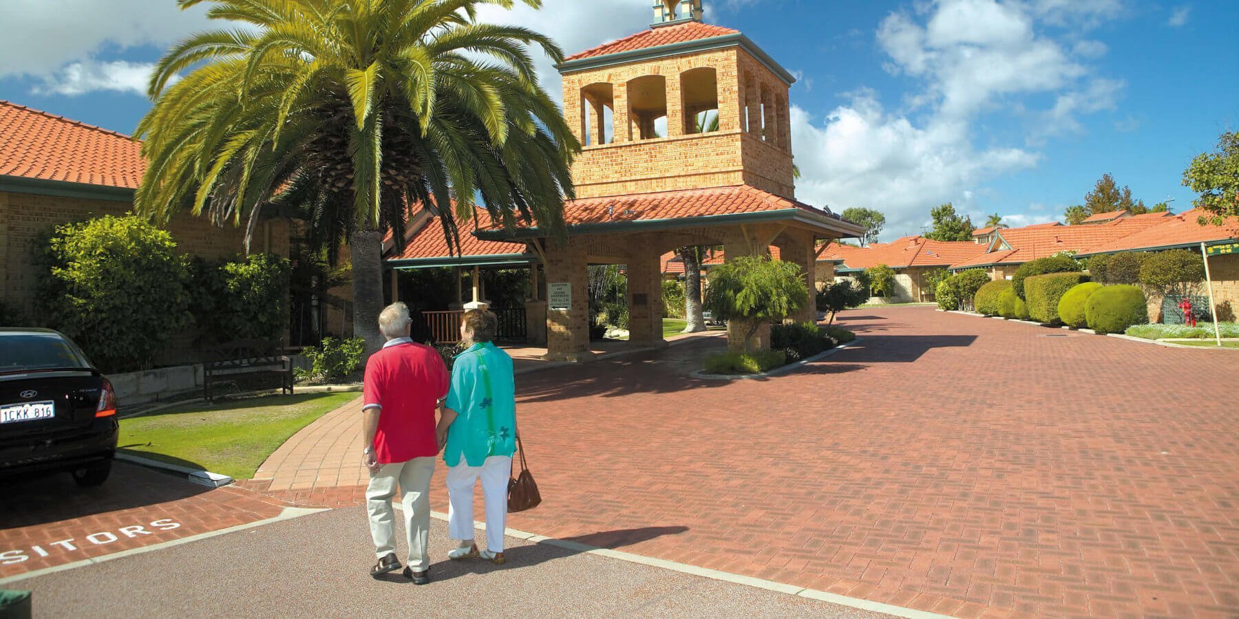 Retired couple walking hand in hand at the entry to St Ives Northshore retirement village
