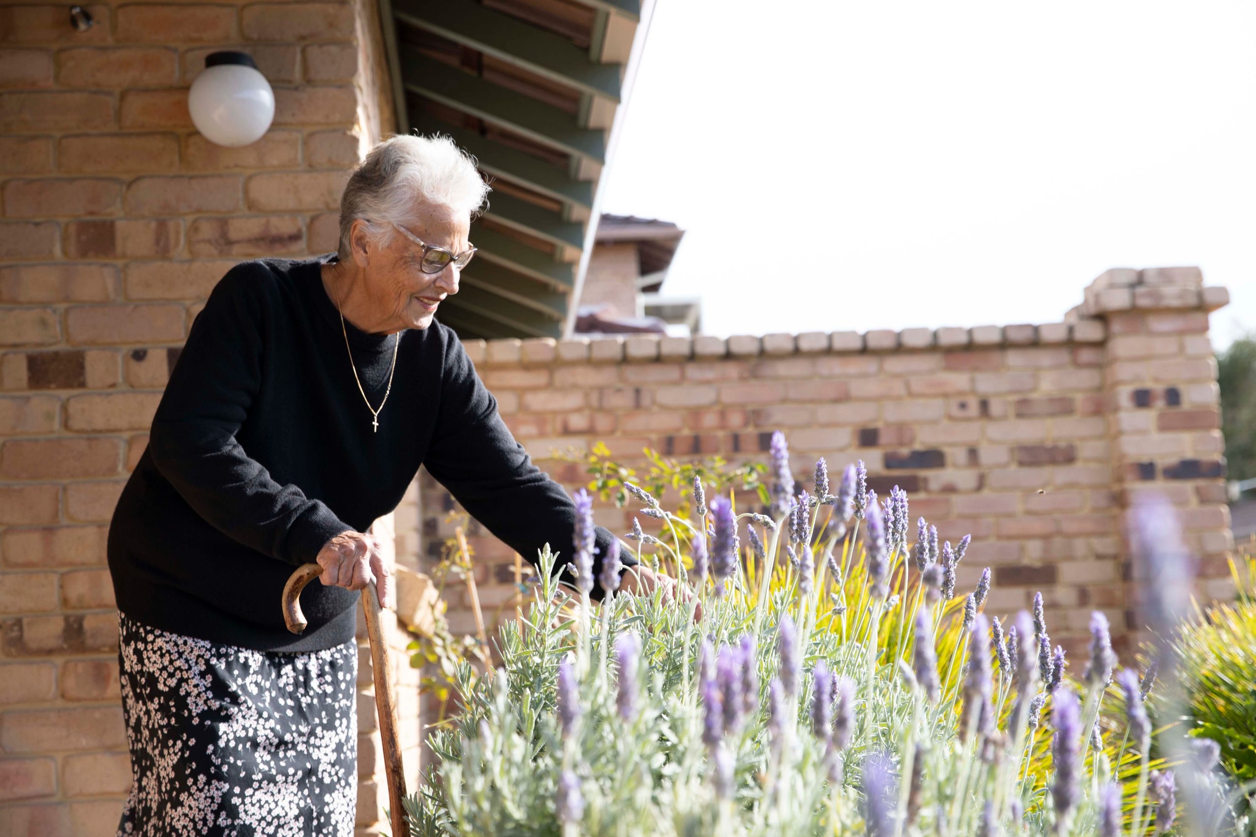 Elderly woman with cane admiring garden at retirement village
